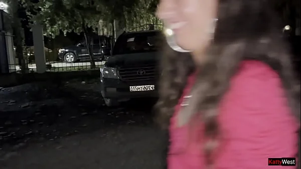 Two girlfriends pee together near a car in a public parking lot